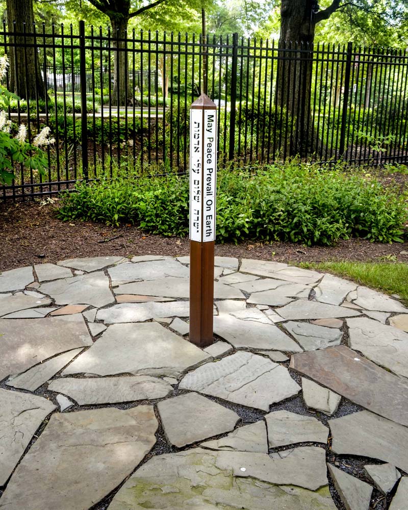 Pole with PEACE written on it in different languages surrounded by flag stones and gardens