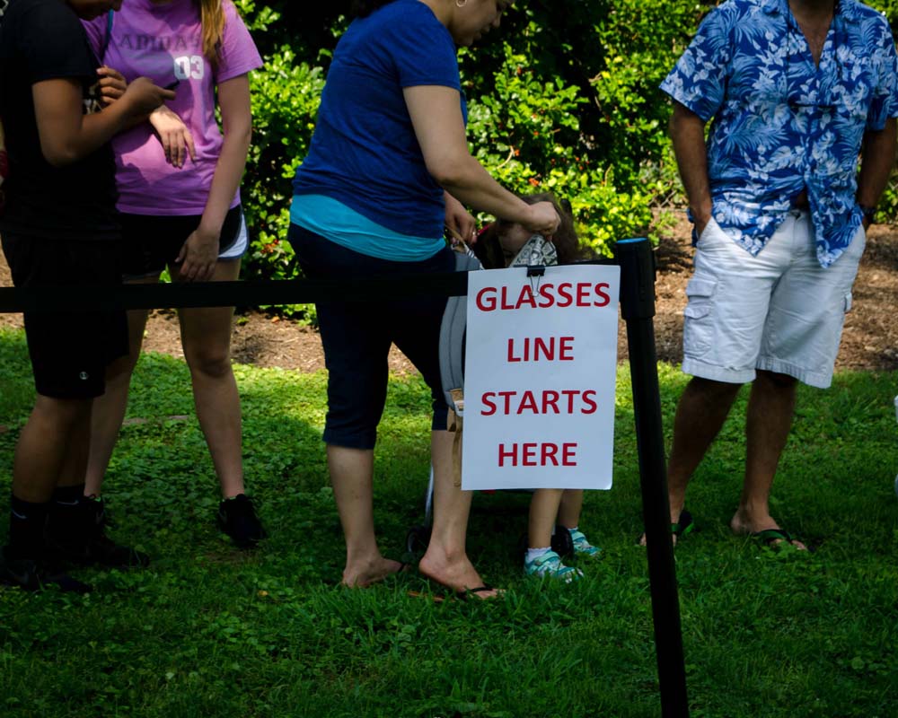 People lining up next to a sign that says Glasses Line Starts Here